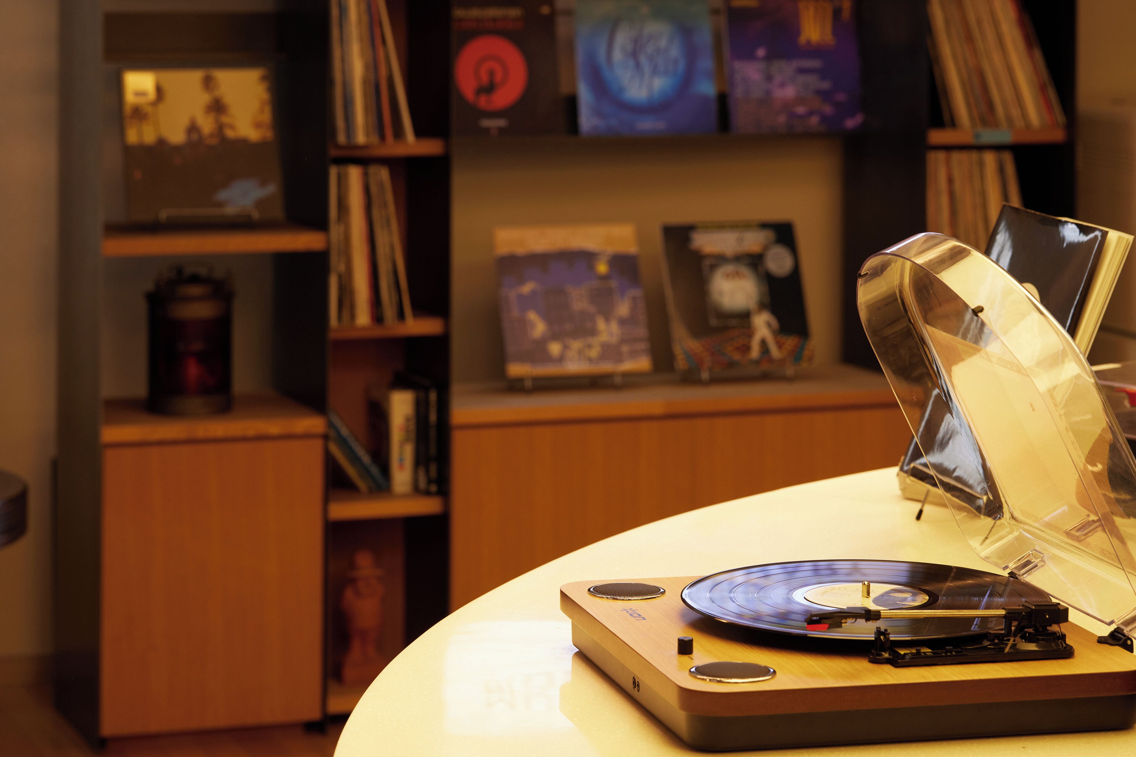 Un giradischi con un disco, un lettore di vinili e una copertina di un disco in primo piano. Sullo sfondo, scaffali pieni di dischi e un mobile in legno.