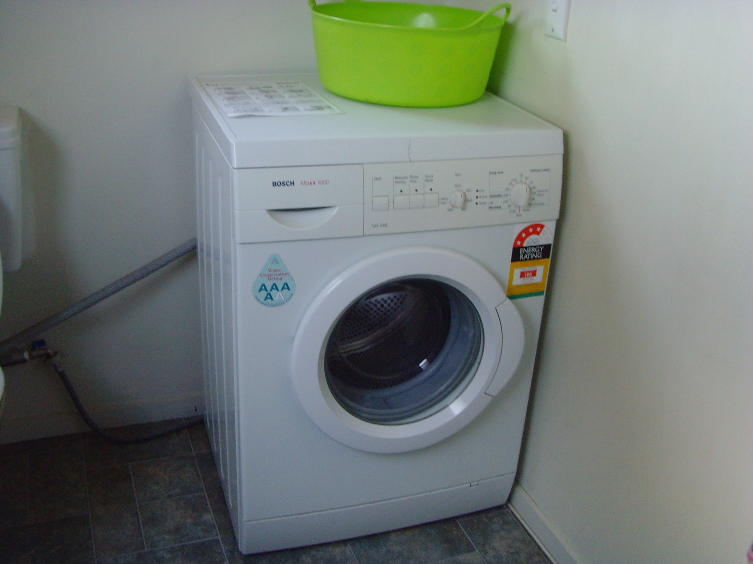 A front-loading washing machine with a green basket on top, an energy rating label, and a control panel with various settings.