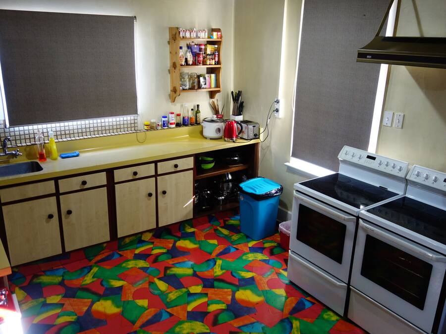 Een keuken met een vloer in verschillende kleuren, een spoelbak, kastjes, een fornuis en een raam.