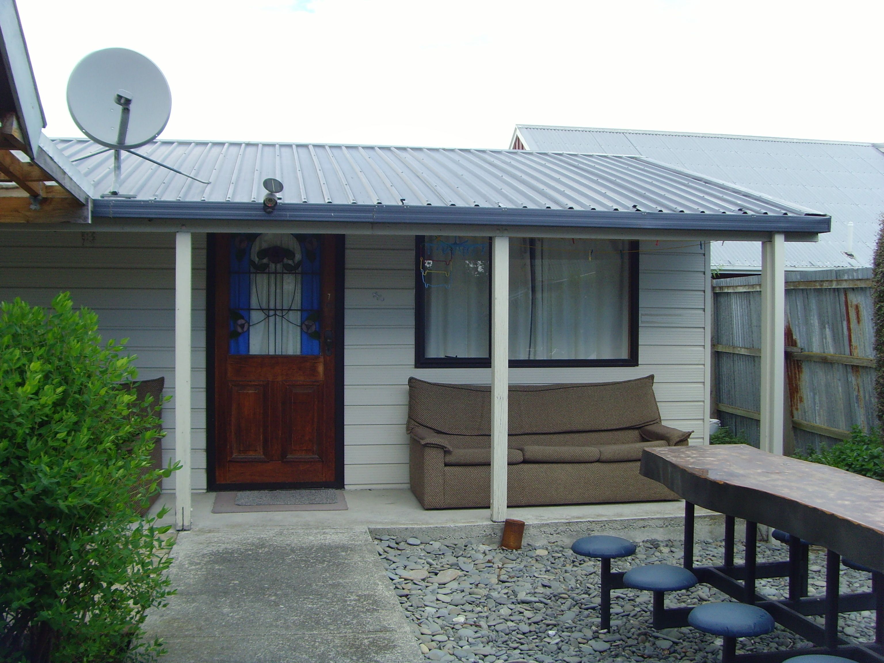 A house with a satellite dish, a wooden door, a porch with a bench, and a table.