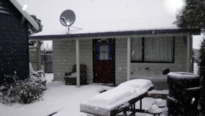 A covered outdoor seating area with a bench and chairs, surrounded by snow. - Big Tree Lodge Methven - Hostel (Methven)