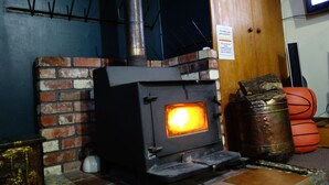 A wood-burning stove with a visible fire, a brick wall, and a wooden door. - Big Tree Lodge Methven - Hostel (Methven)