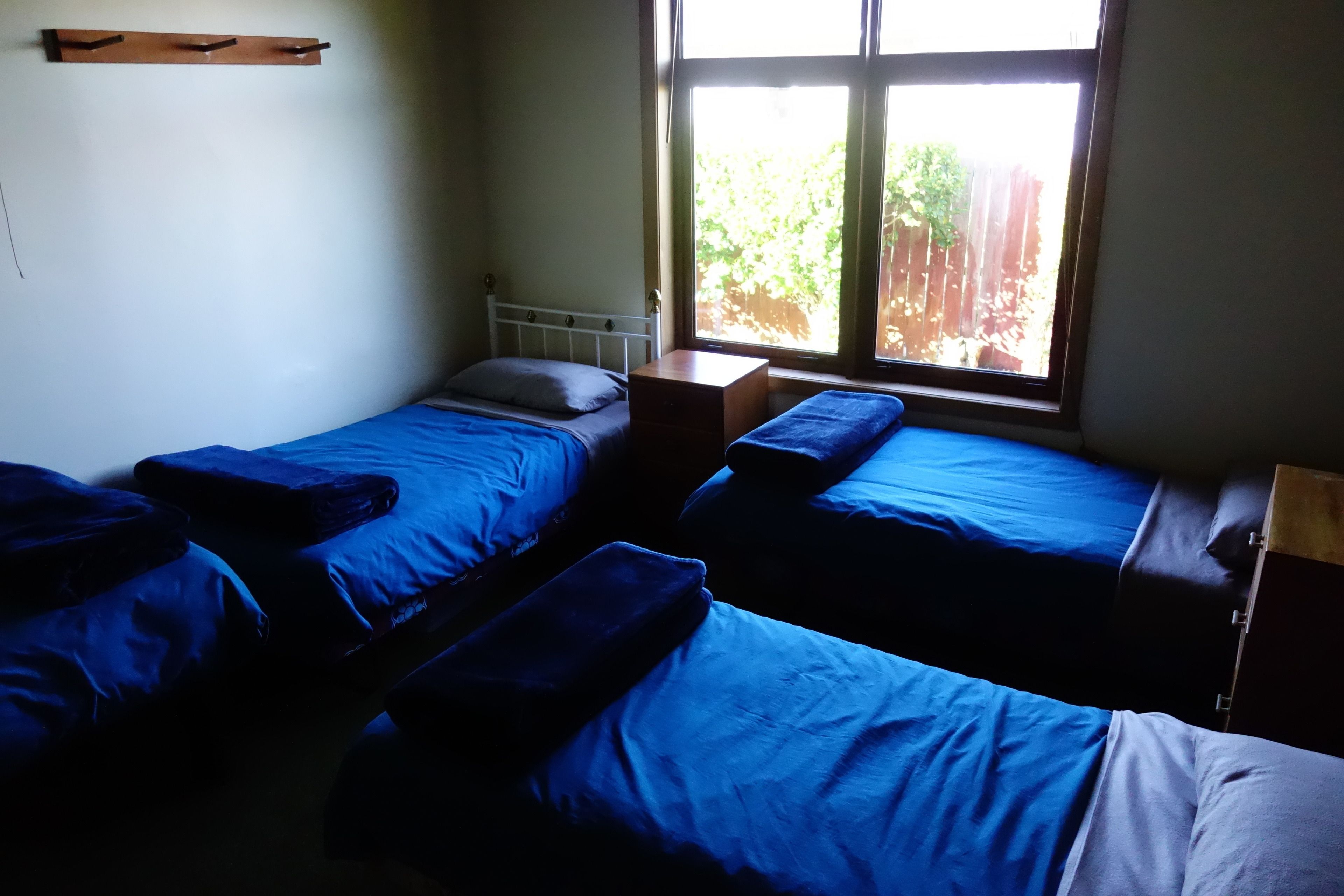 A dormitory room with two beds, a window, and a small wooden shelf.