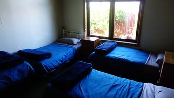 A dormitory room with two beds, a window, and a small wooden shelf.