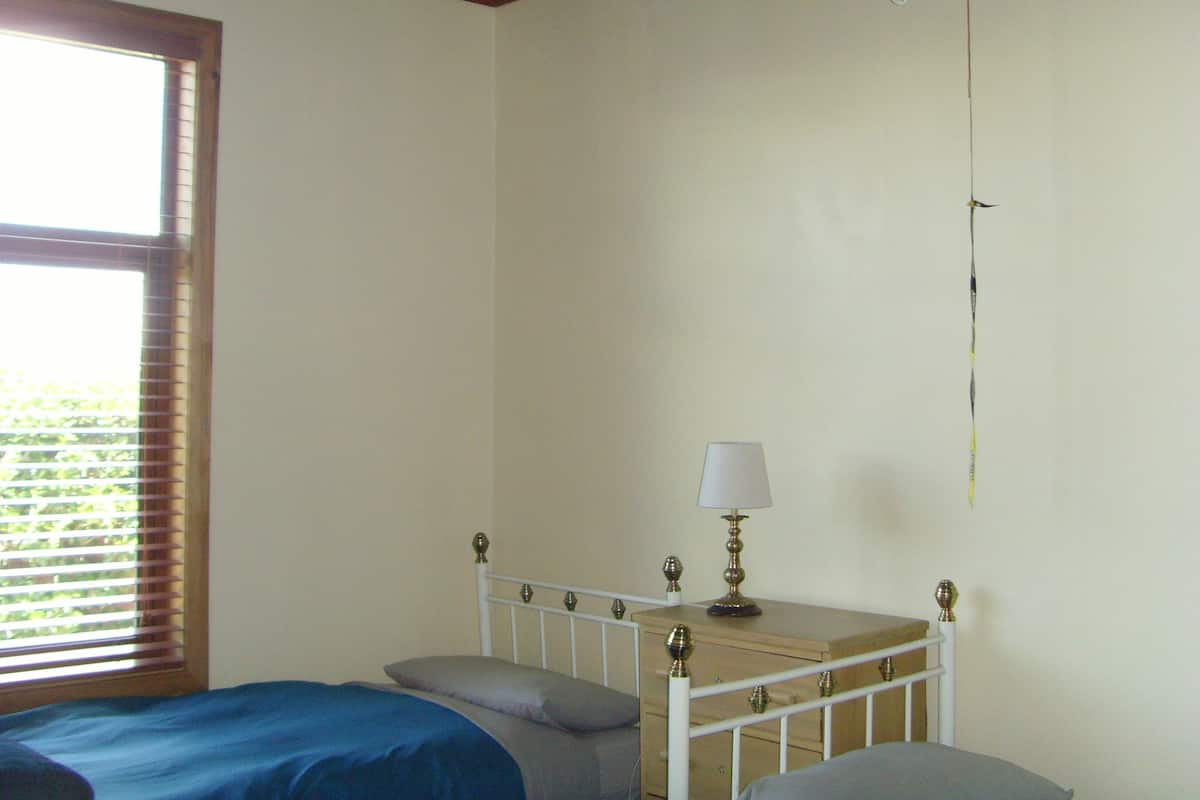 Un dormitorio con cama, una mesita de noche con lámpara y una ventana con persianas.