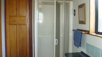 Un baño con puerta de madera, cabina de ducha, lavamanos y espejo.