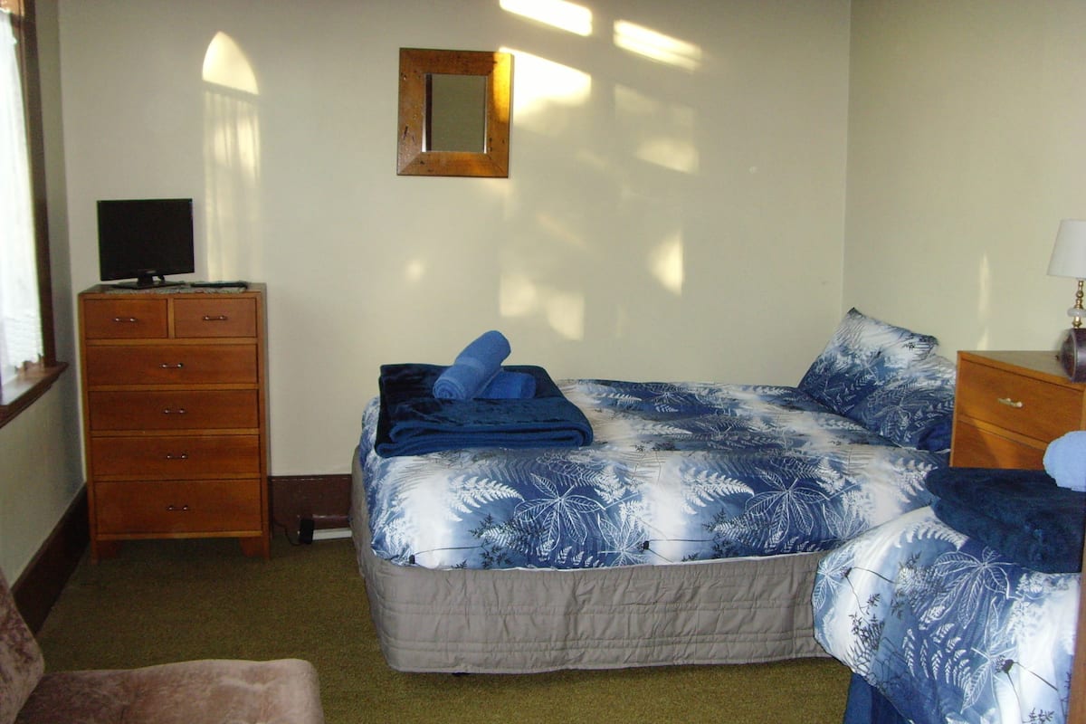 Un dormitorio con una cama, un aparador, un televisor encima del aparador y una ventana con cortinas.
