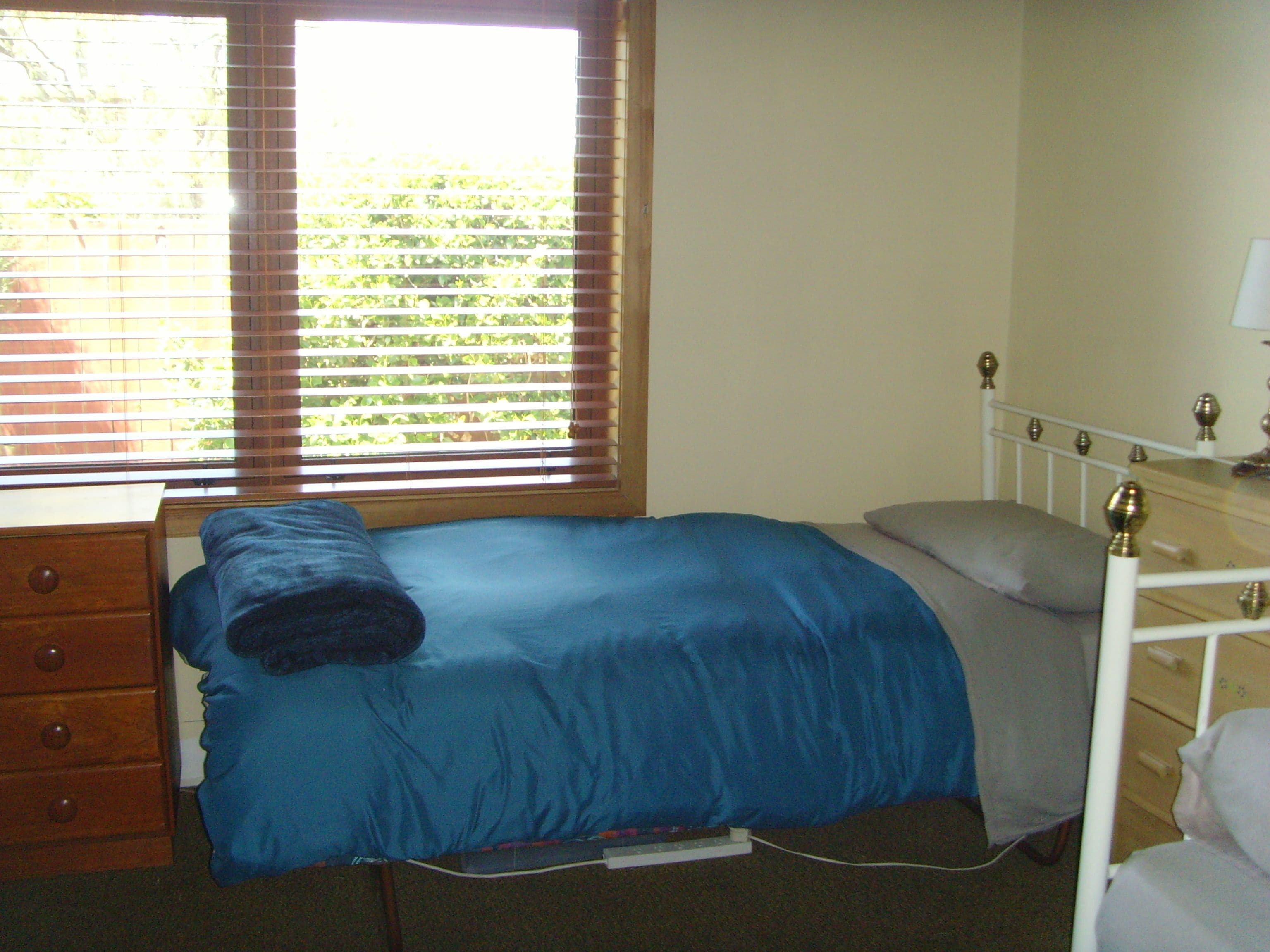 Un dormitorio con una cama individual, un aparador de madera y una ventana con persianas.