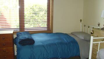 Un dormitorio con una cama individual, un aparador de madera y una ventana con persianas.