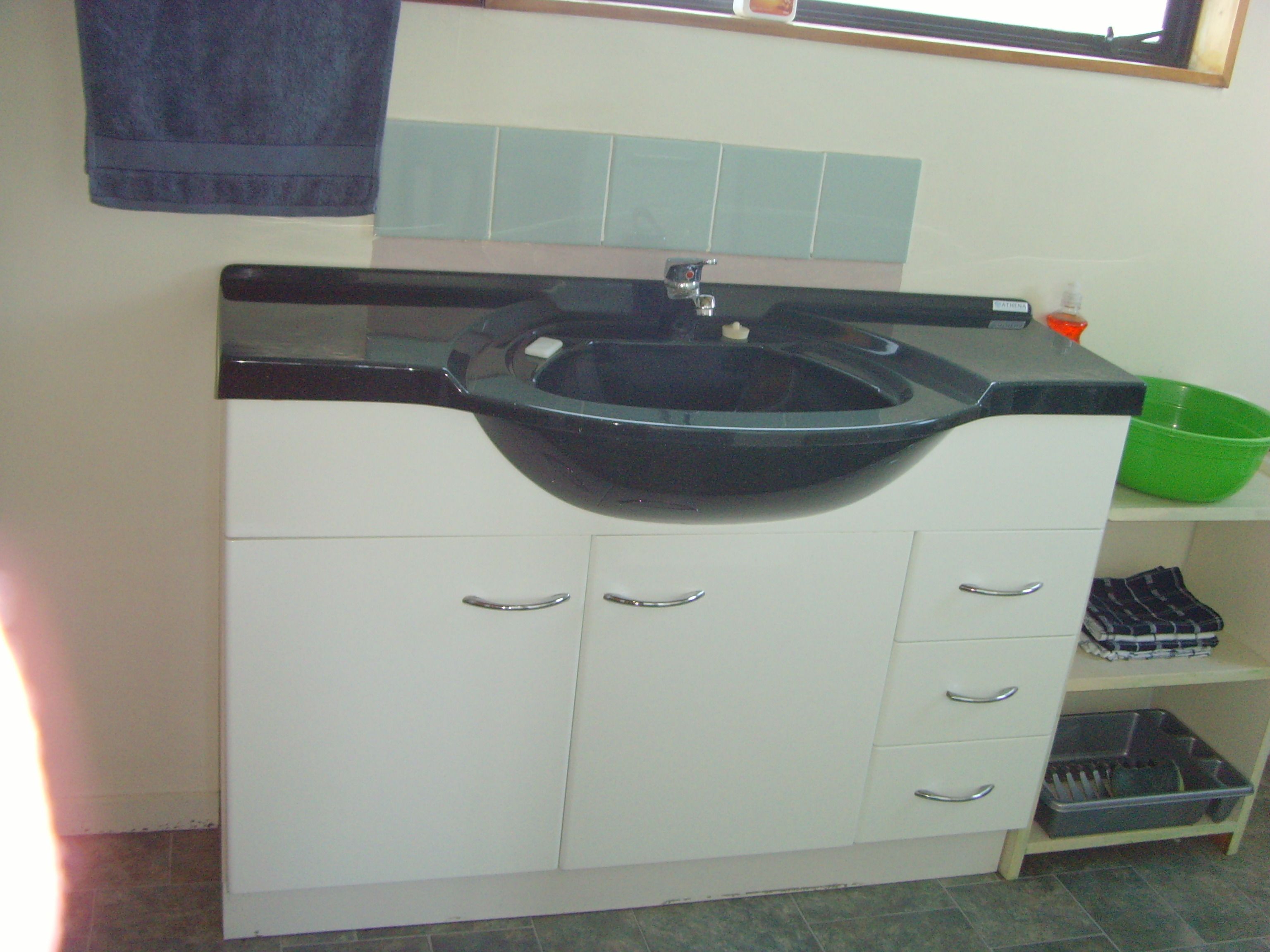 Un baño con un lavabo negro, armarios blancos y un cuenco verde sobre el mostrador.