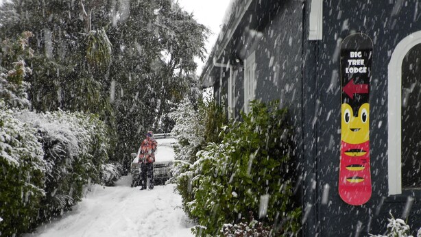 A snowy residential street with a house featuring a snowboard sign on the door. - Big Tree Lodge Methven - Hostel (Methven)