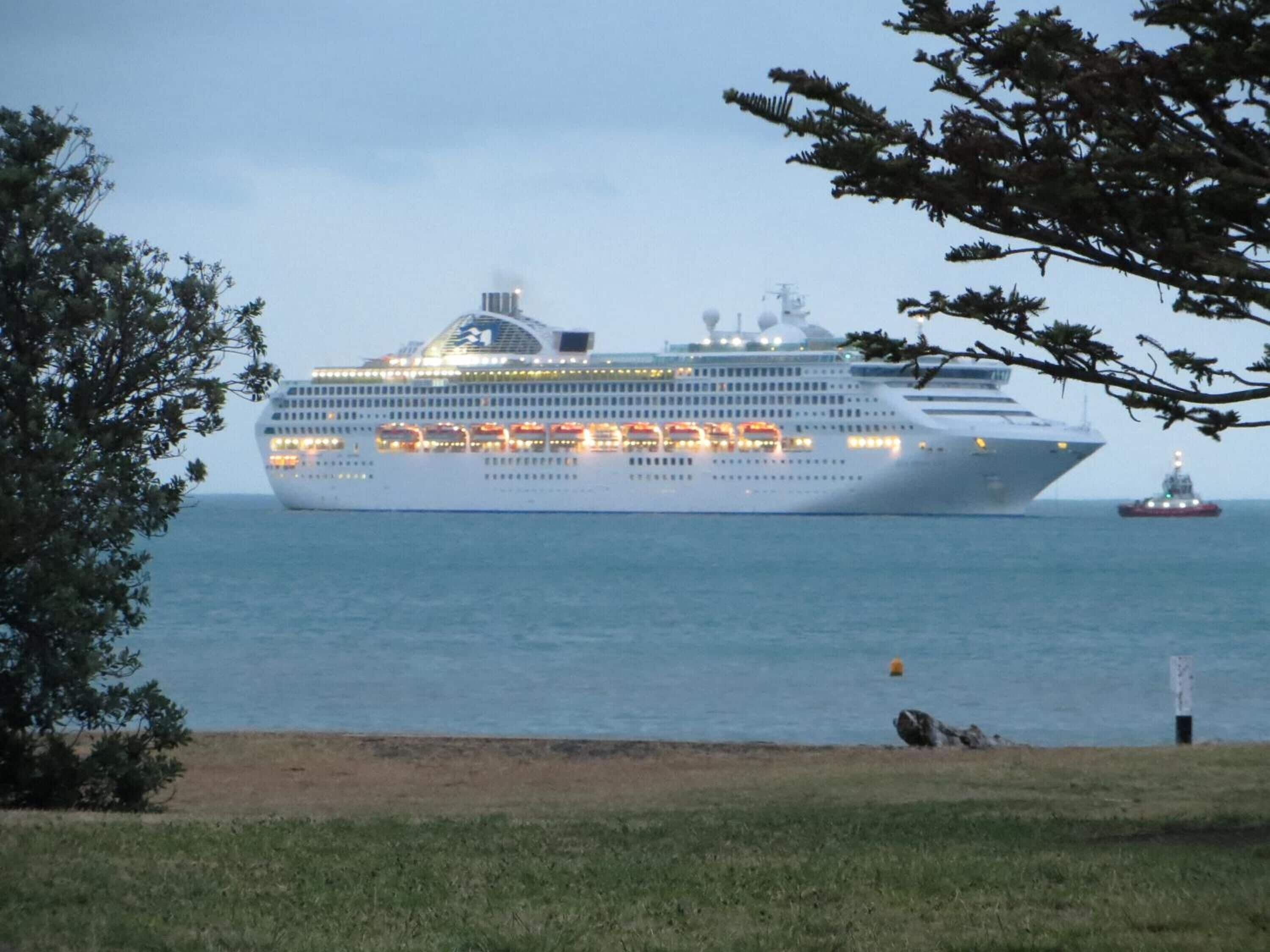 Un gran crucero amarrado en el puerto, con un remolcador cerca.