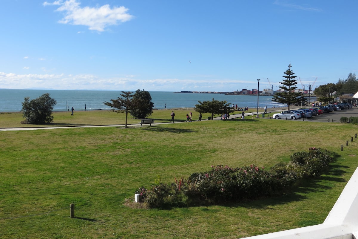 A grassy park area with a walking path, a bench, and a view of the sea.