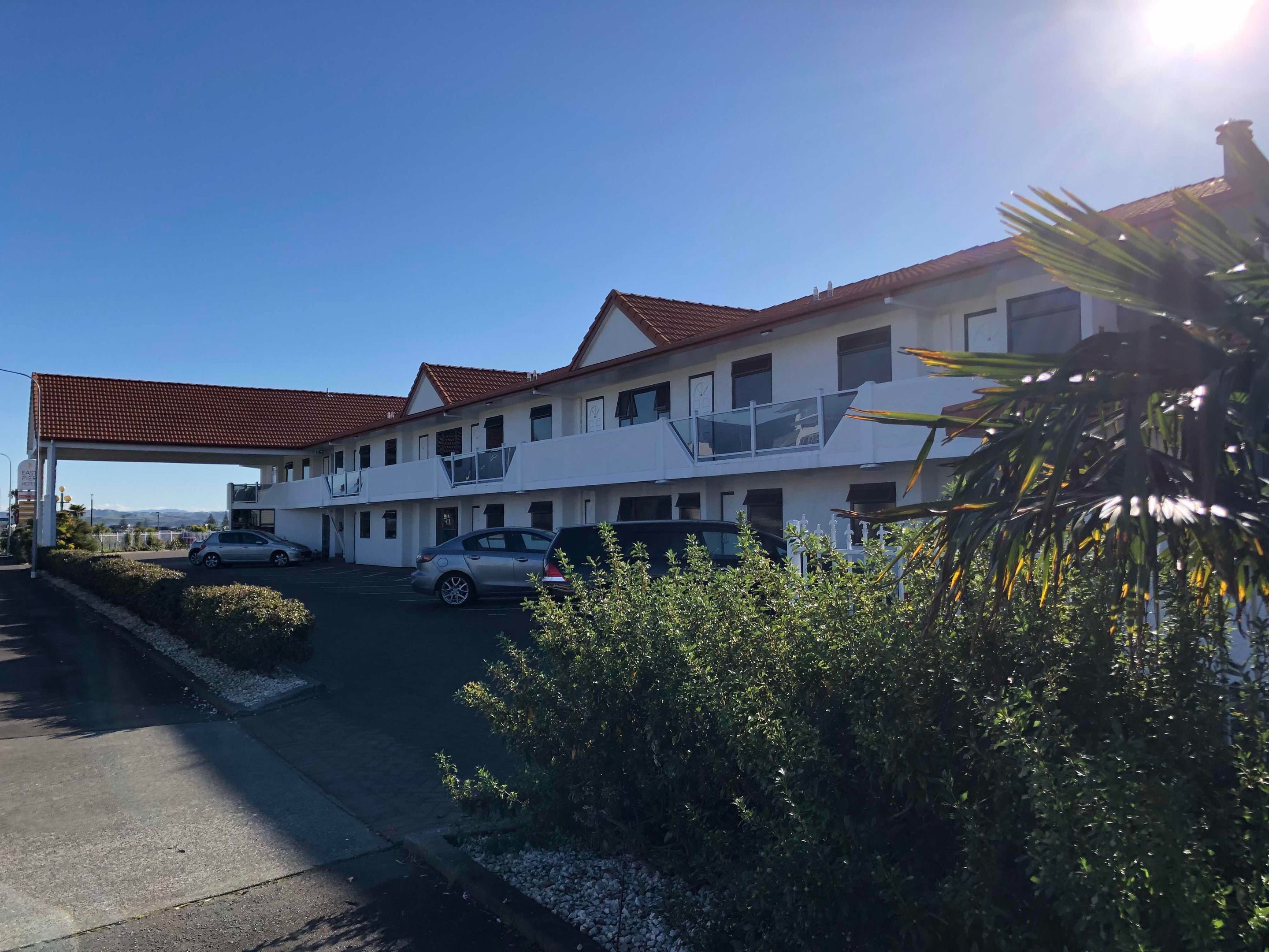 Un motel con una estructura de dos pisos, una zona de estacionamiento techada y vistas del paisaje circundante.