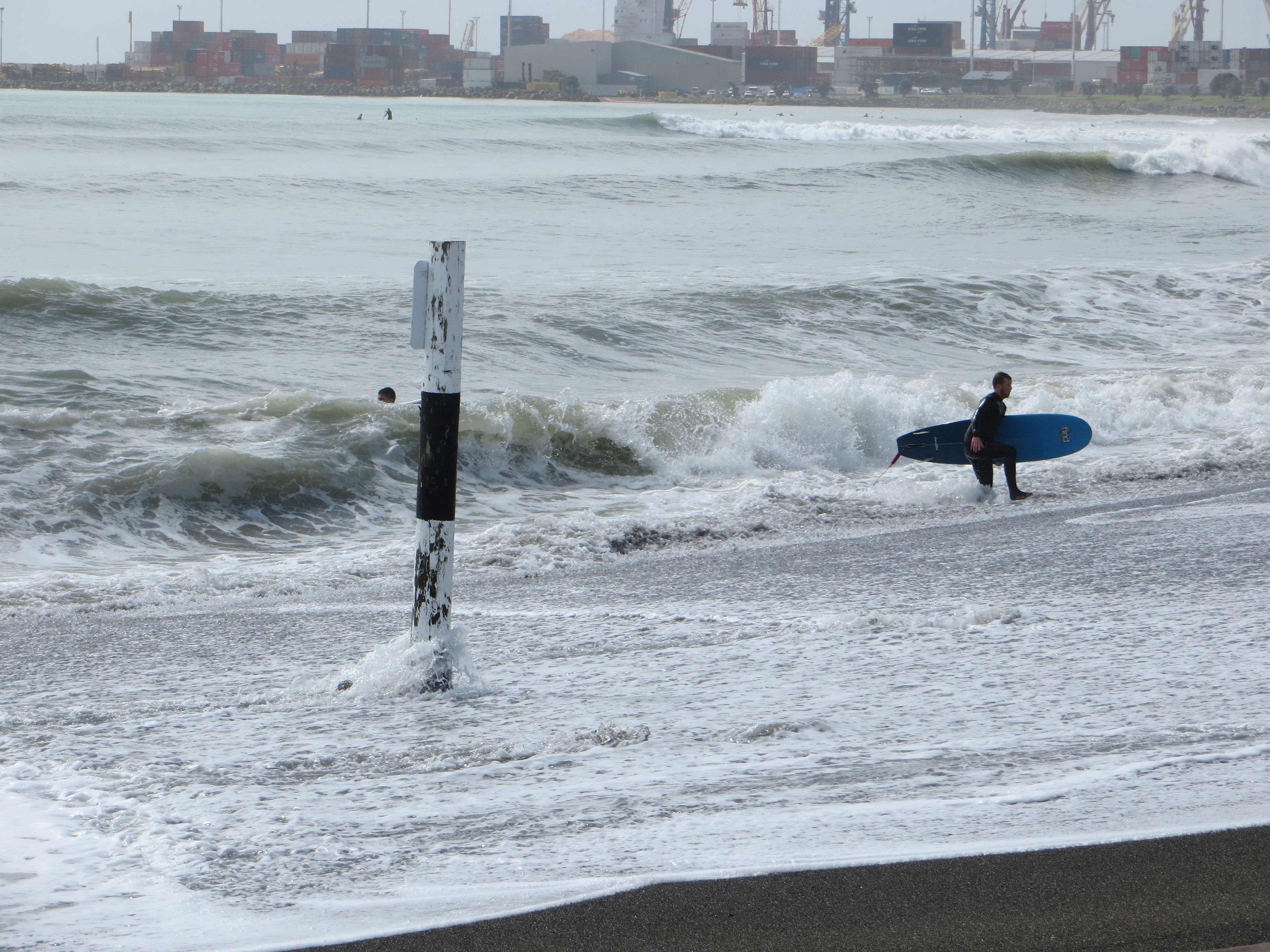 Une plage avec des vagues et un surfeur qui porte une planche de surf.