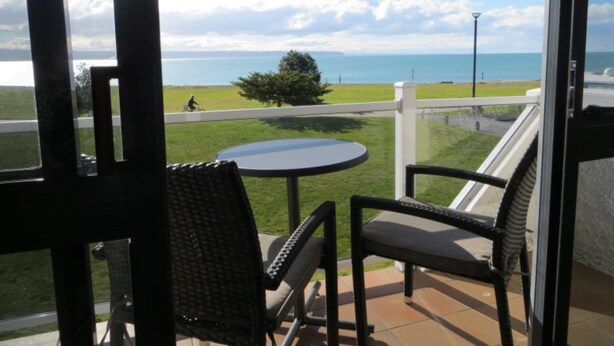 Un balcón con mesa y sillas, con vistas a una zona verde y al mar.