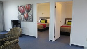 Una habitación de hotel con dos camas, un área de comedor con mobiliario de mimbre y un cuadro en la pared.