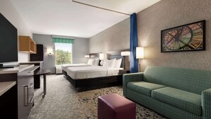 A hotel room with a bed, a desk, a green sofa, and a painting on the wall. - Home2 Suites by Hilton Florence, SC (Florence)