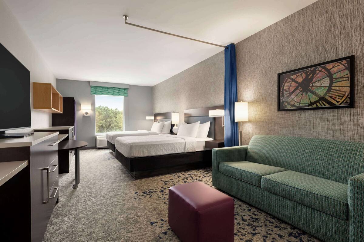 A hotel room with a bed, a desk, a green sofa, and a painting on the wall.