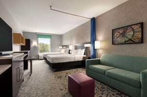 Una habitación de hotel con cama, escritorio, sofá verde y un cuadro en la pared.