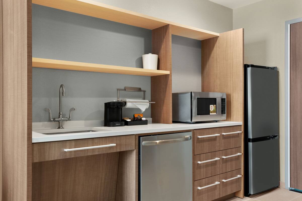 A modern kitchen with a stainless steel refrigerator, a microwave, a coffee maker, and wooden cabinets.
