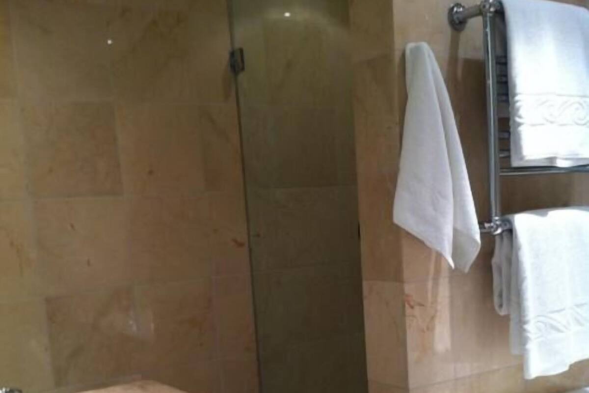 Un baño con lavamanos de mármol, ducha con cerramiento de vidrio y un perchero con varias toallas.