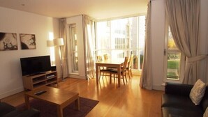 Una sala de estar con televisor, mesa de centro de madera, sofá y mesa de comedor con sillas.