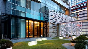 A modern building with large glass windows, a patterned facade, and a well-maintained garden area with planters and seating.