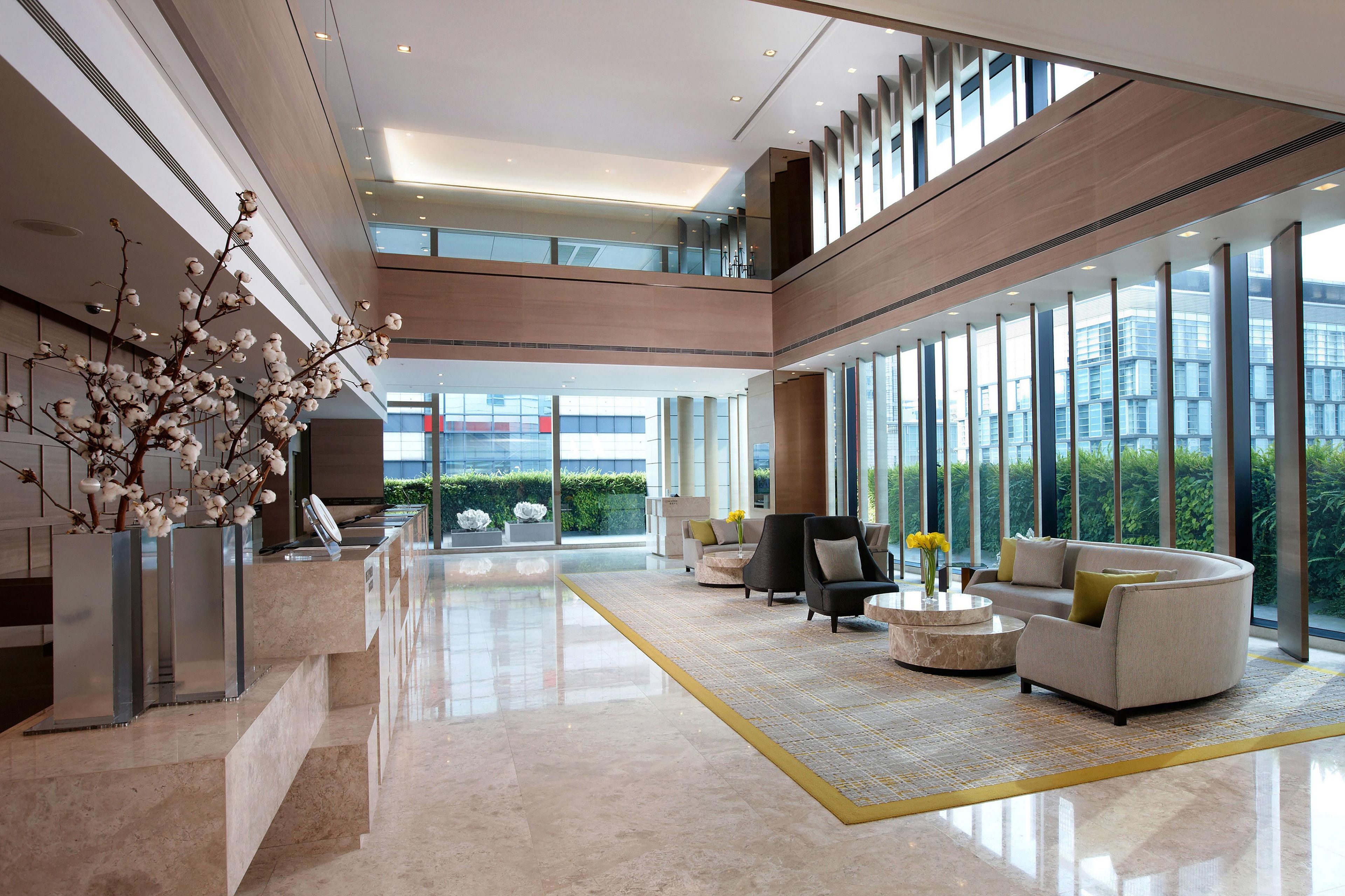 A spacious lobby with a high ceiling, a reception desk, seating area, and large windows offering a view of the outdoors.