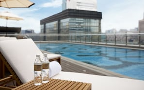 Ein Poolbereich auf dem Dach mit Liegestühlen und zwei Wasserflaschen auf einem Holztisch.
