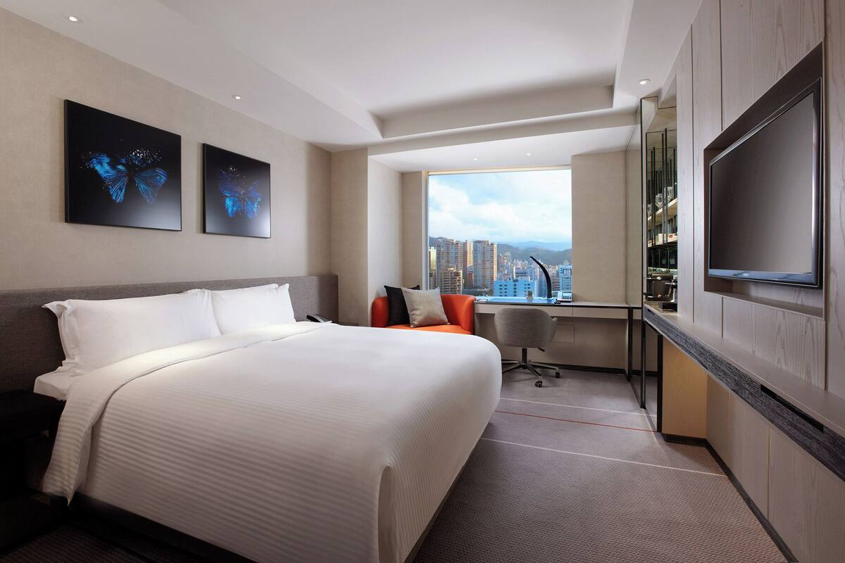 A hotel room with a large bed, a desk, a chair, a TV, and a city view.