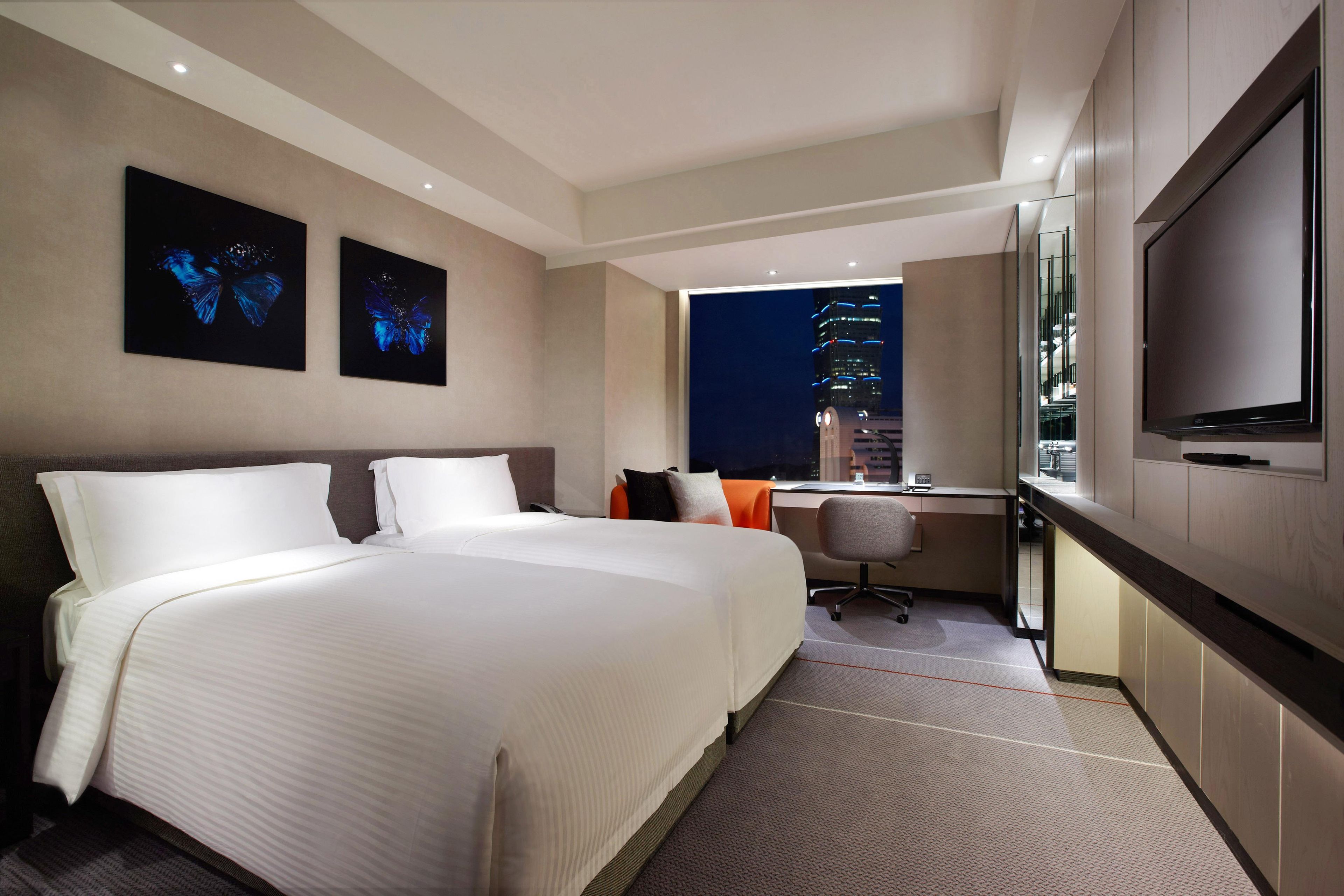 Habitación de hotel con una cama grande, un escritorio con silla, un televisor de pantalla plana y dos cuadros con motivo de mariposas en la pared.