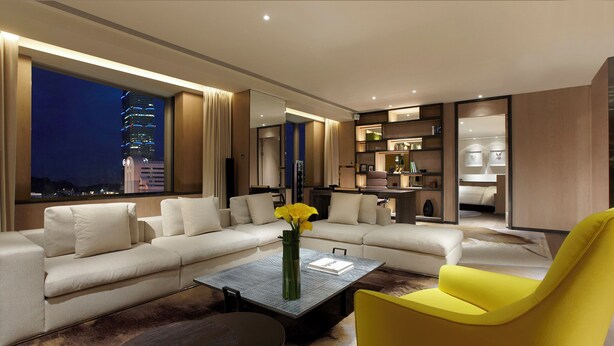 A modern living room with a sofa, a yellow armchair, a coffee table, and a view of a cityscape at night.