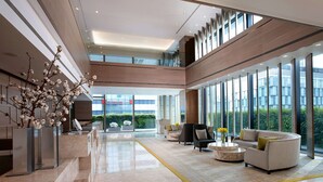 A spacious lobby with a high ceiling, large windows, and a central seating area with modern furniture.