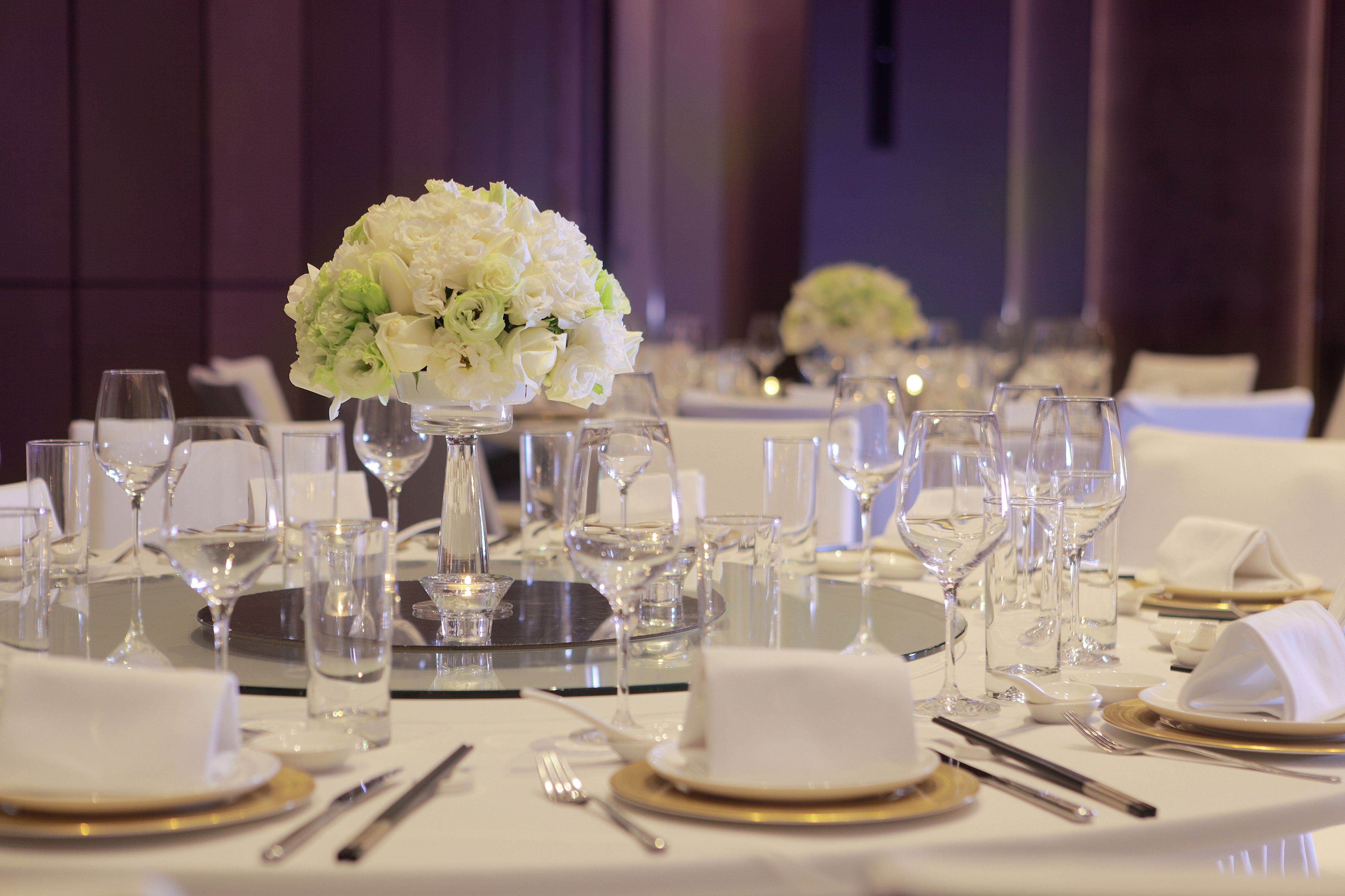 A table set for a formal event with white tablecloths, clear glassware, and gold-rimmed plates.