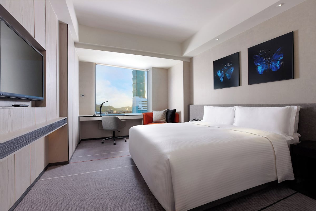 A hotel room with a bed, a desk, a chair, a TV, and two butterfly paintings on the wall.