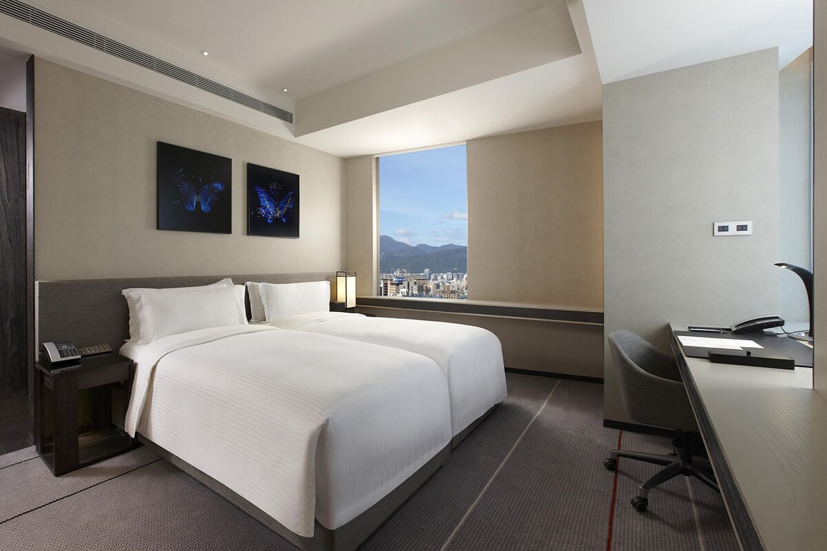 A hotel room with a large bed, a desk, and a view of a cityscape.