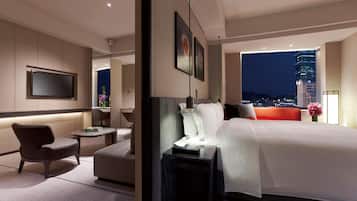 A modern hotel room with a large bed, a seating area, a flat-screen TV, and a city view.