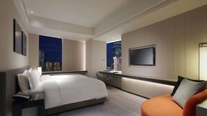 A modern hotel room with a bed, a desk, a chair, and a TV on the wall.