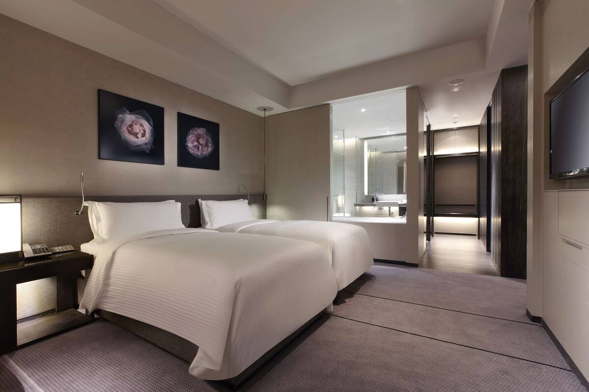 A modern hotel room with a large bed, bedside tables, a flat-screen TV, and a bathroom with a glass shower.