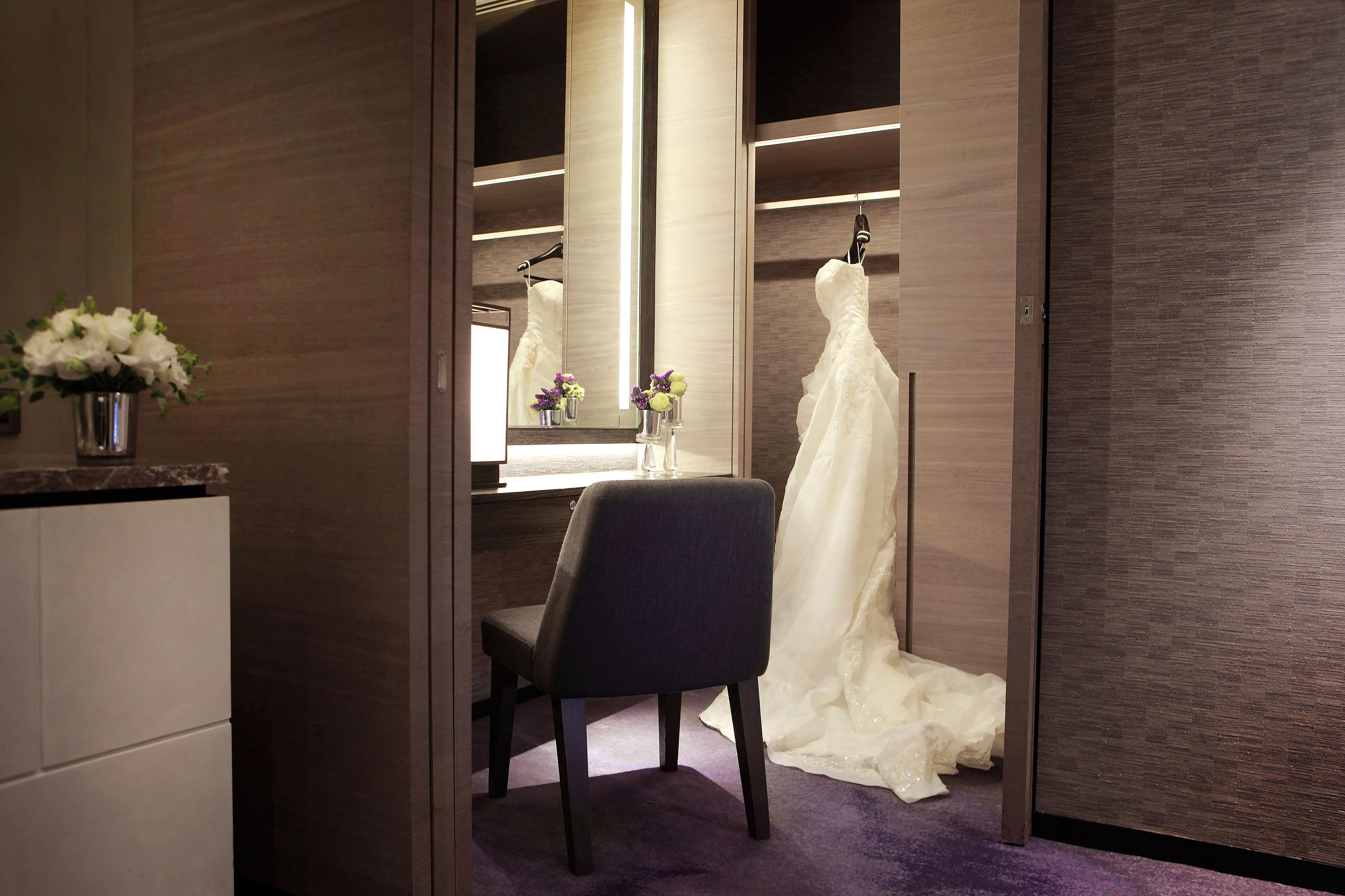 A hotel room with a walk-in closet, a vanity with a mirror, and a wedding dress on a hanger.