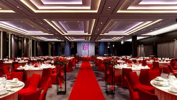 A banquet hall with round tables, red chairs, and a red carpet.