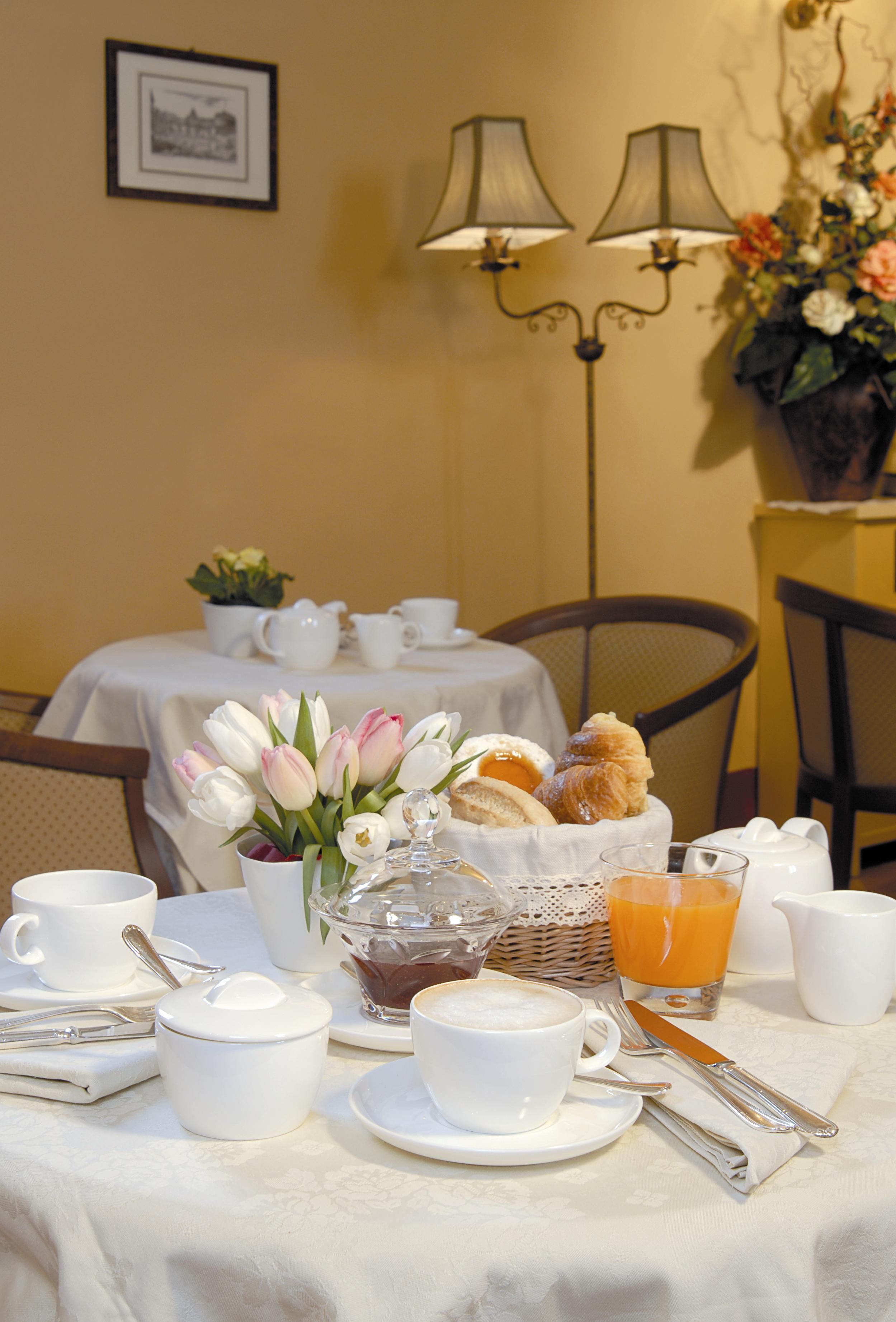 A breakfast table set with white cups, a glass of orange juice, a basket of bread, and a vase of tulips.