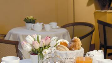 A breakfast table set with white cups, a glass of orange juice, a basket of bread, and a vase of tulips.