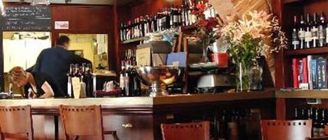 A bar with a counter, chairs, and shelves of bottles.