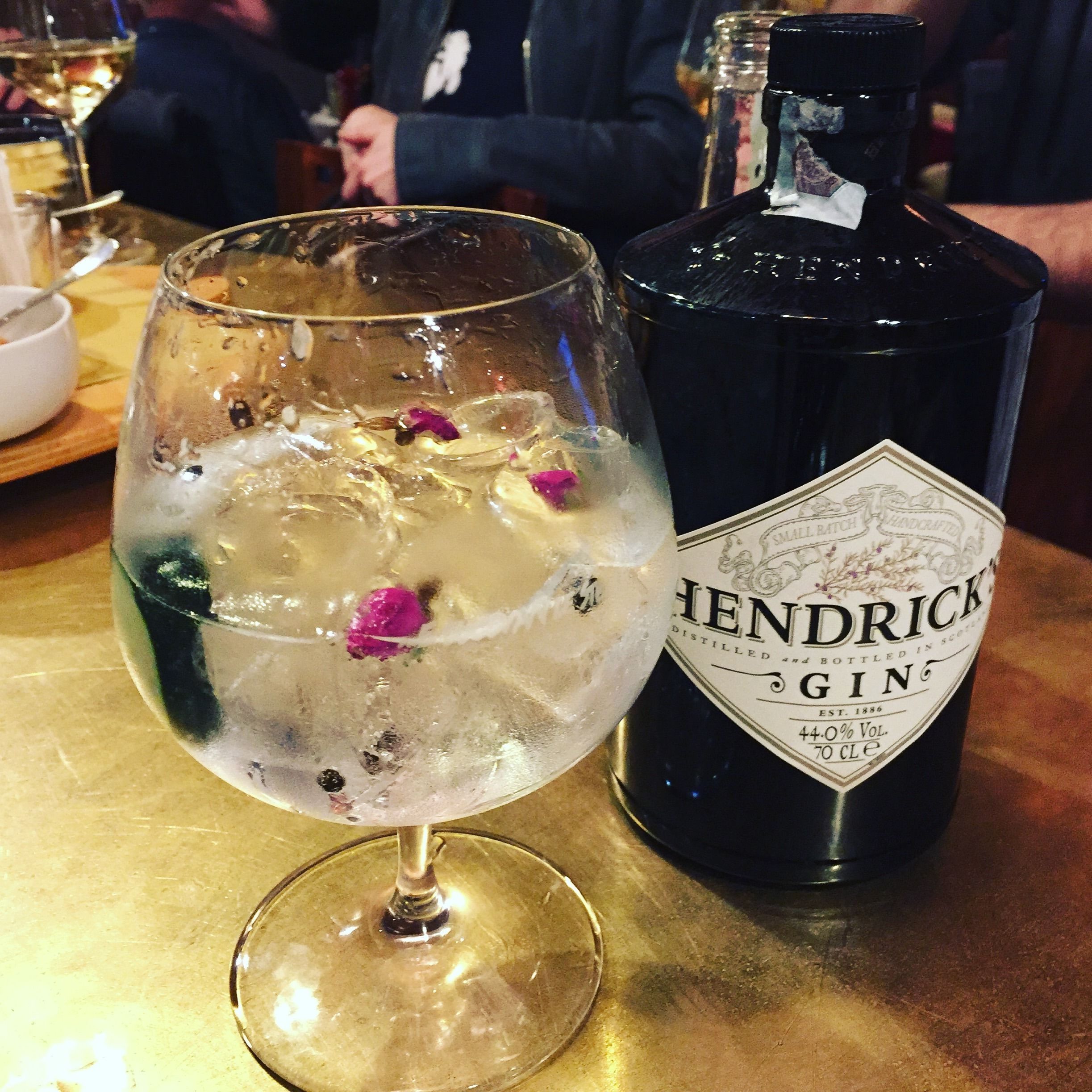 Une bouteille de gin Hendrick's et un verre contenant des glaçons et des pétales de fleurs.