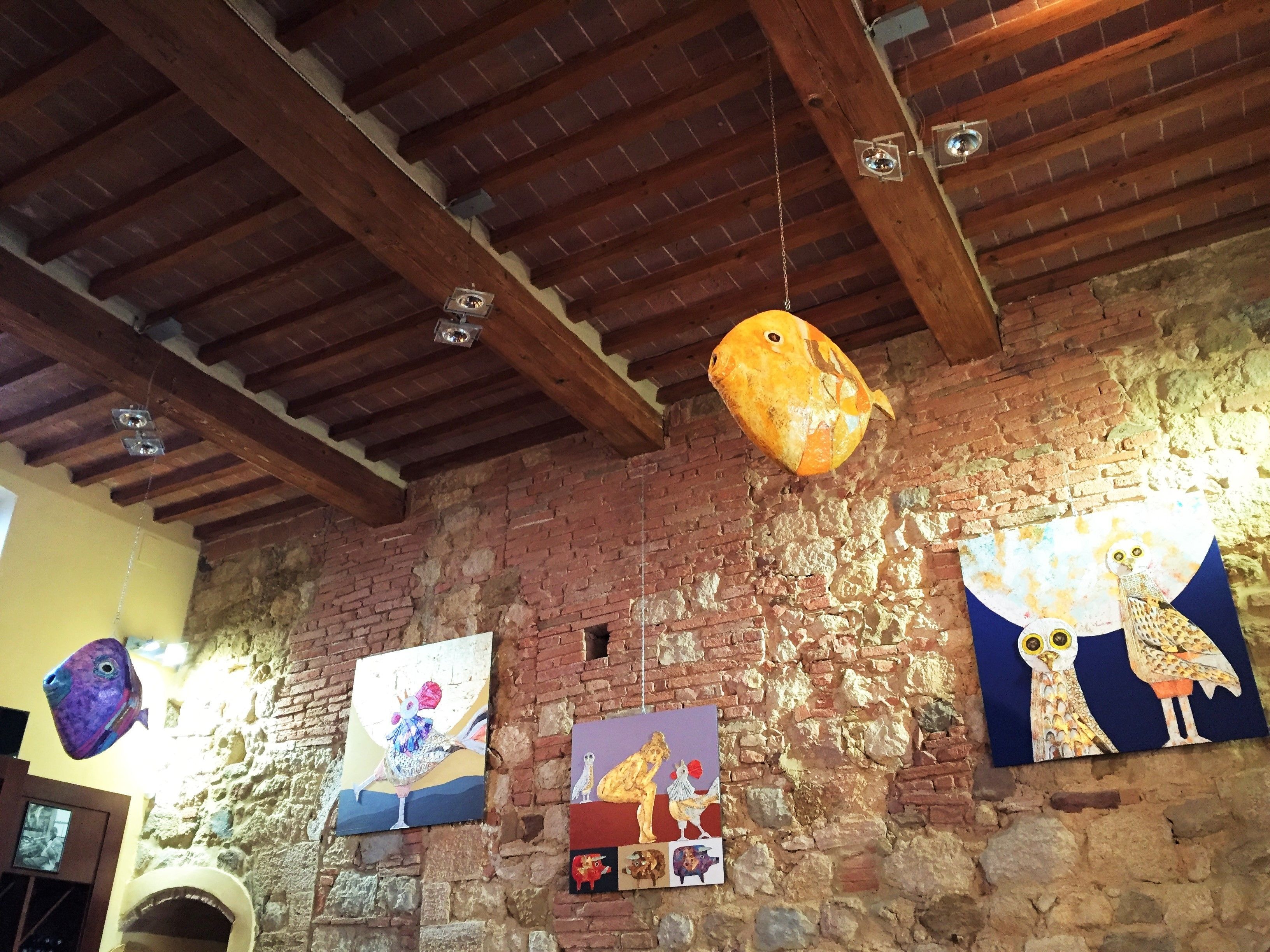 A rustic room with exposed brick walls, wooden beams on the ceiling, and various artworks displayed on the walls.
