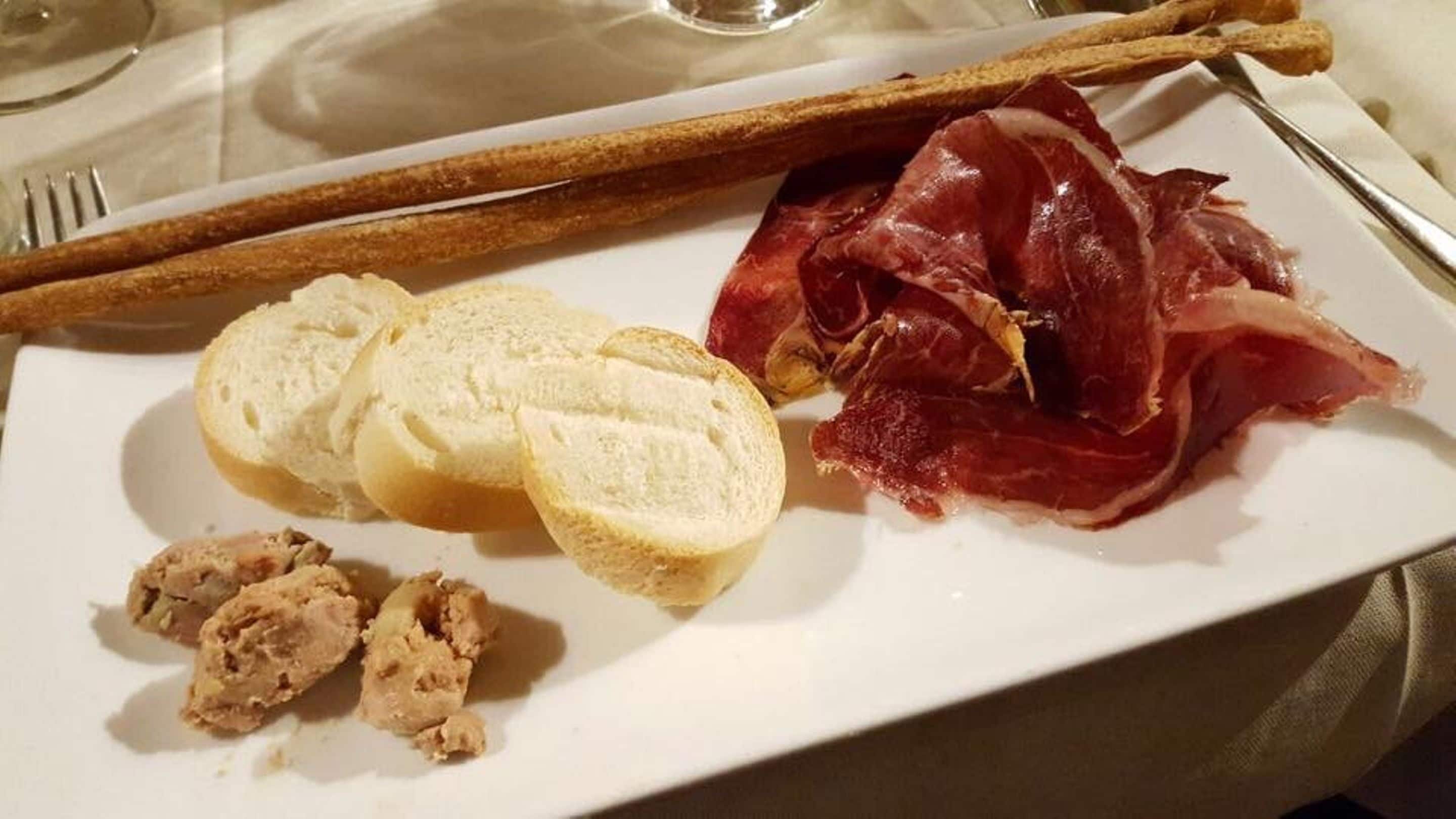 Ein Teller mit Brot, Prosciutto und einer kleinen Fleischportion.