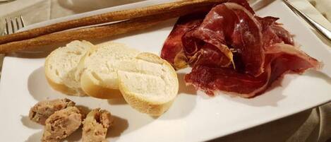 Ein Teller mit Brot, Prosciutto und einer kleinen Fleischportion.