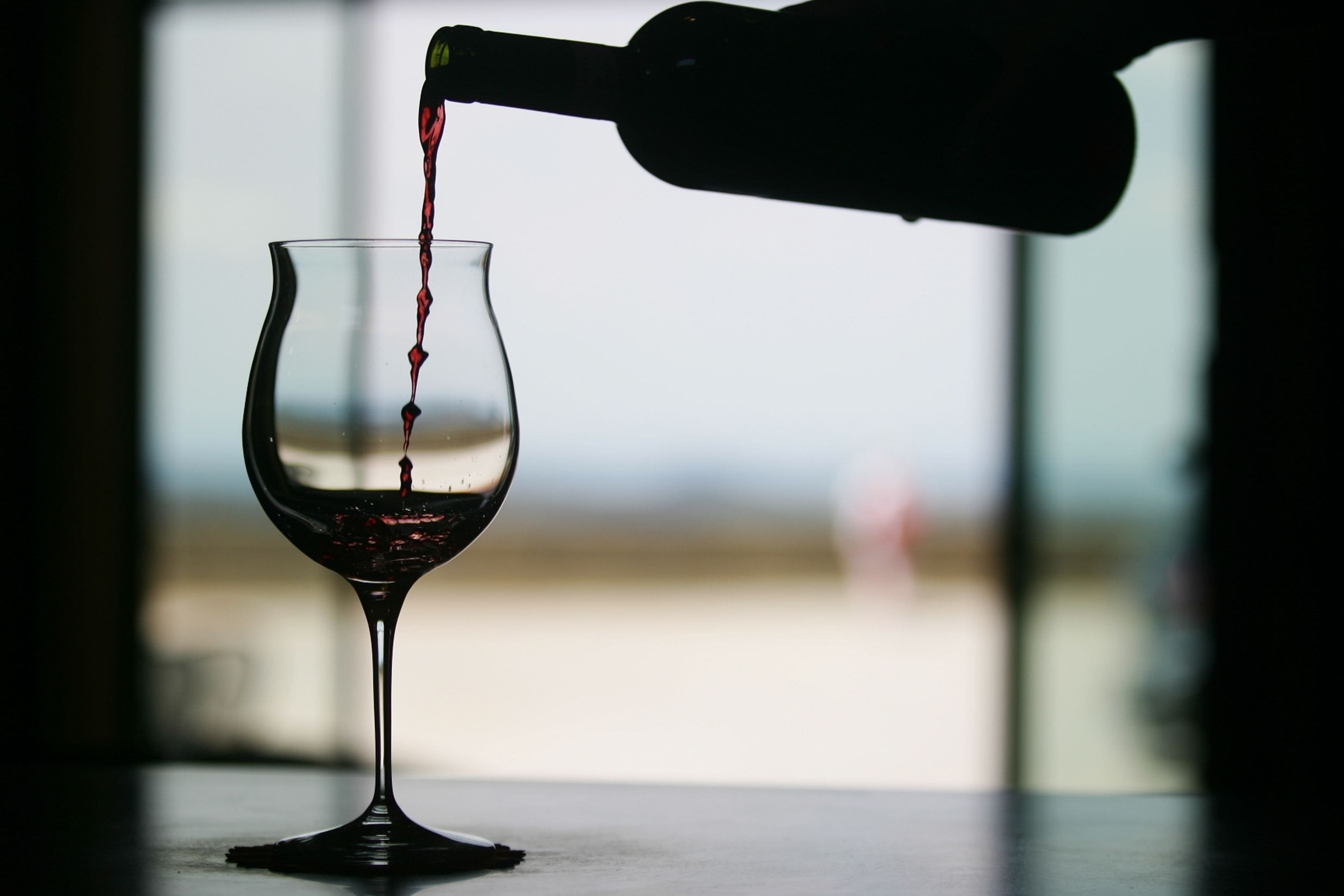 A wine bottle pouring red wine into a glass.